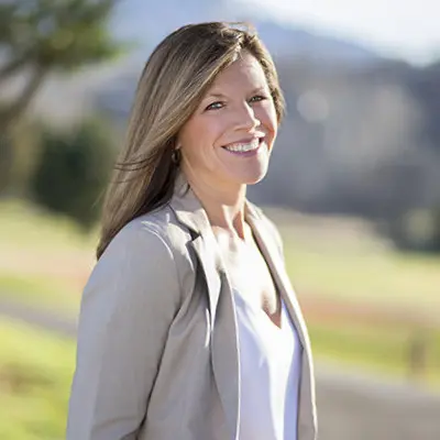 Smiling blonde woman outdoors in a beige jacket, looking confident and happy