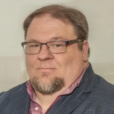 Professional headshot of man with glasses, goatee, and checkered blazer