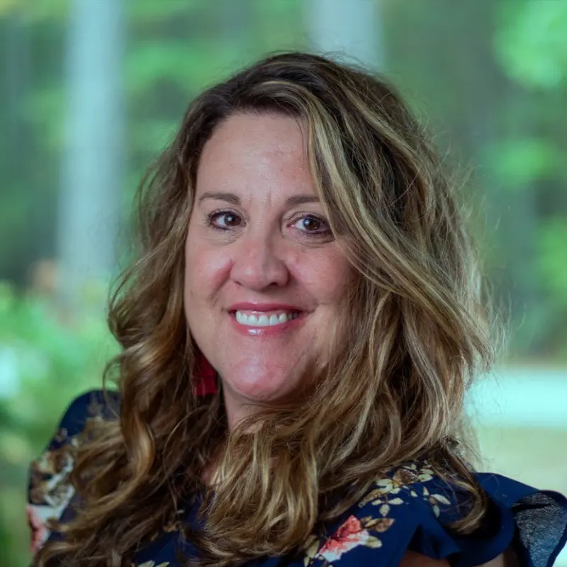 Smiling professional woman headshot with long highlighted brown hair, floral top