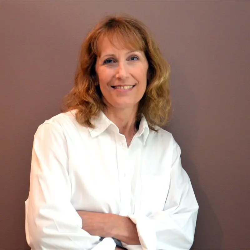 Smiling professional woman, blonde hair, white shirt, arms crossed, standing confidently