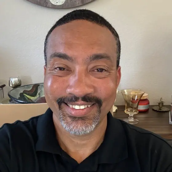 Smiling African American man, black polo shirt, gray goatee, professional headshot
