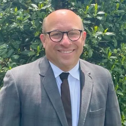Smiling bald man with glasses, grey suit, dark tie, green bush background