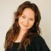 Smiling woman, long wavy brown hair, blue eyes, black top, professional headshot