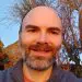 Smiling bald man with beard and blue eyes outdoors at golden hour