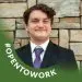 Smiling young man in black suit, purple tie, #OPENTOWORK against stone wall