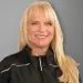 Blonde woman with bangs smiling in black athletic jacket with white trim