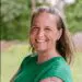 Smiling woman with gray hair, green shirt, and arm tattoo outdoors