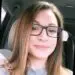 Smiling young woman with long brown hair and black glasses in car