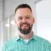 Smiling man with beard in green plaid shirt. Professional headshot for business