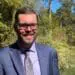 Smiling professional man with beard, glasses, blue suit in outdoor nature