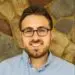 Professional headshot: smiling man with glasses, beard, light blue shirt