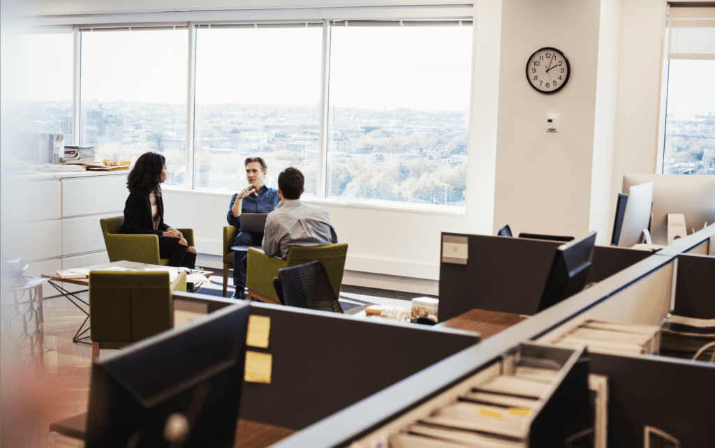 Three professionals discuss business in a modern office with city views