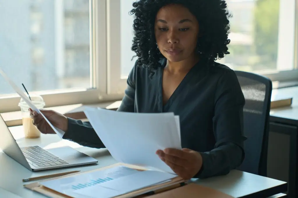 Focused Black woman reviewing business documents and charts at office desk